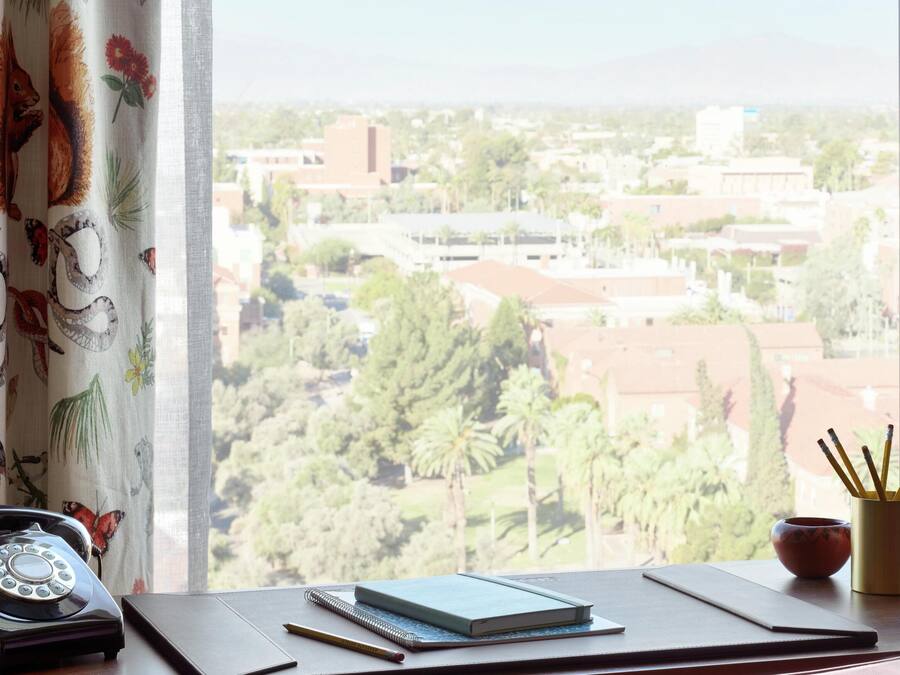 A desk with a rotary phone, a notebook, and a pencil, overlooking a cityscape with buildings and greenery.