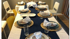 Taula de menjador preparada amb plats, gots i coberts, envoltada de cadires.