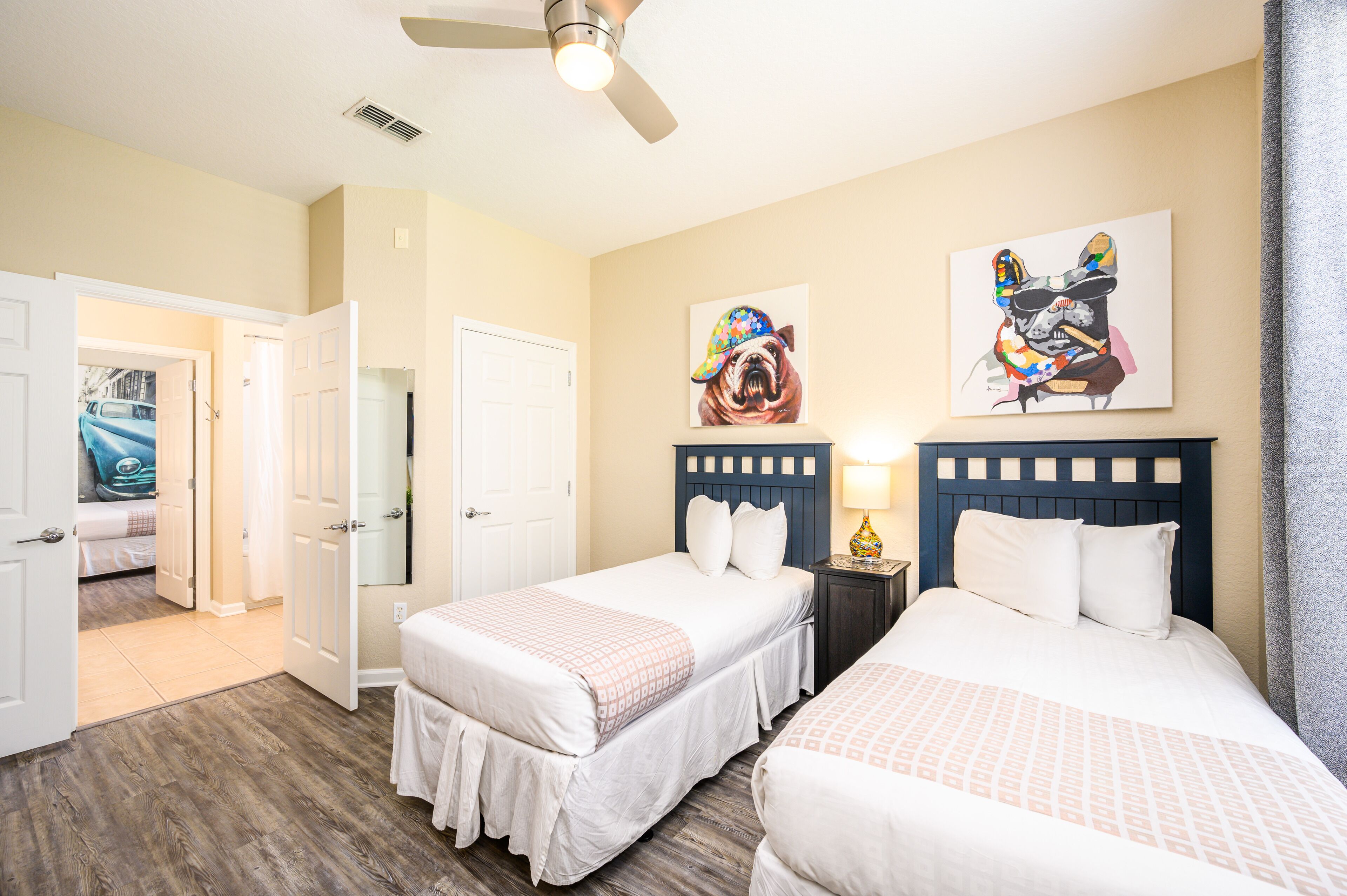 A hotel room with two beds, a ceiling fan, and artwork on the walls.