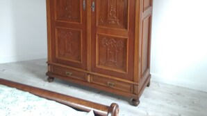 A wooden wardrobe with intricate carvings, a bed with a floral-patterned bedspread, and a wooden ceiling. - Ferienwohnung Albert, 2 Schlafzimmer, 90 Quadratmeter (Hauenstein)