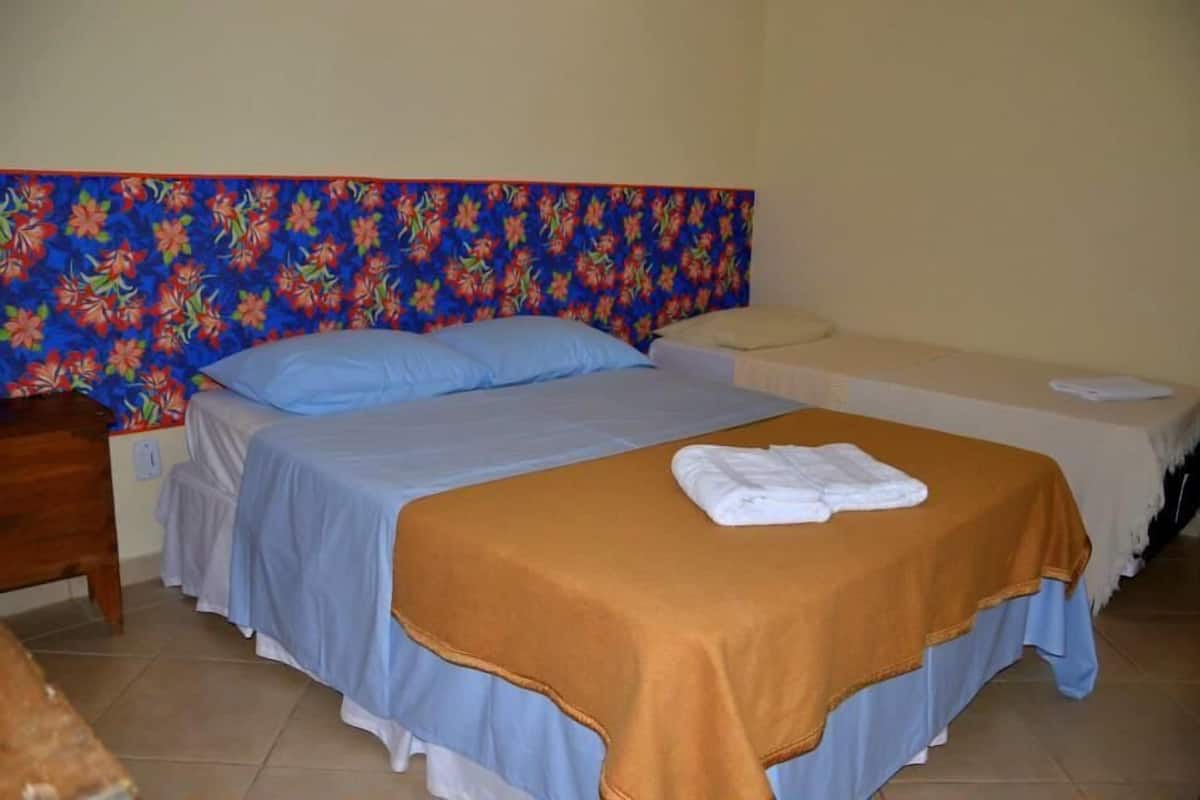 A hotel room with a bed, a smaller bed, a nightstand, and a headboard with a floral pattern.