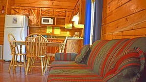 Un accogliente interno di una baita con un tavolo da pranzo in legno, sedie, un divano e un angolo cottura che include un frigorifero e un forno a microonde.