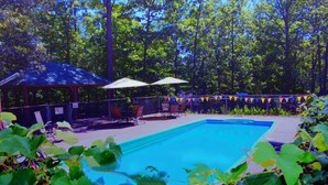 Una piscina rettangolare con superficie d'acqua azzurra, circondata da una zona patio recintata con sedute all'aperto e ombrelloni.
