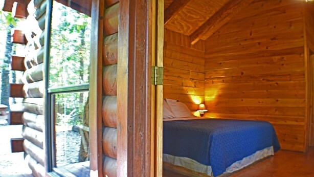 Una camera in una baita di legno, con un letto, una finestra e un comodino con una lampada.