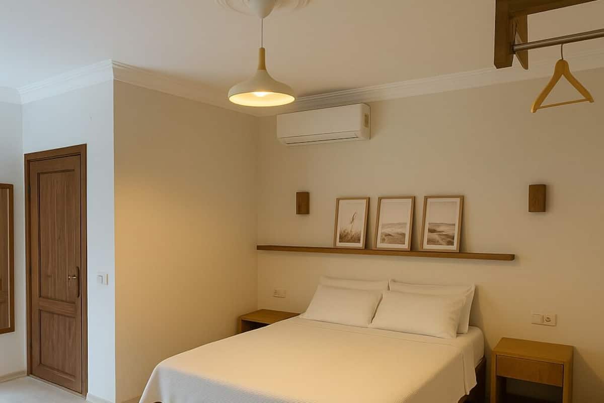 Une chambre à coucher comprenant un lit, des tables de chevet, un luminaire suspendu, un climatiseur fixé au mur et une armoire en bois.