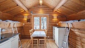 Uma cabana aconchegante com interior de madeira, uma mesa de jantar e duas beliches.