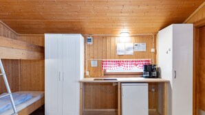 Uma cozinha compacta com paredes de madeira, uma geladeira branca, uma pia pequena e toalha de mesa xadrez.