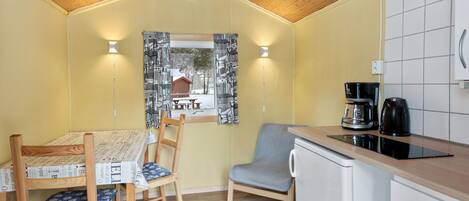 A compact kitchen with a dining table, chairs, a coffee maker, and a window with curtains.