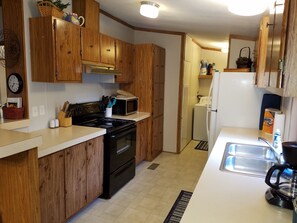 Compact kitchen with a stove, microwave, refrigerator, sink, faucet, and coffee maker.
