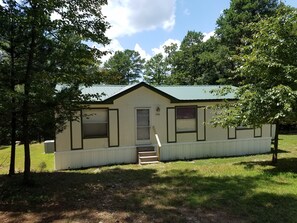 Cozy home with a gabled roof and small front porch, set amidst a grassy area with trees.