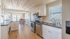 A modern kitchen with white cabinets, stainless steel appliances, and a wooden ceiling.