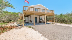 A two-story wooden house with a balcony, an American flag, and a sandy driveway.