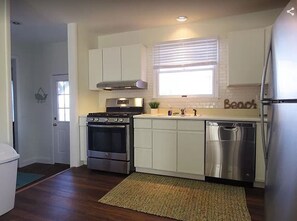 Kitchen features a stove, oven, dishwasher, and refrigerator, with a window above the sink and a small plant on the countertop.