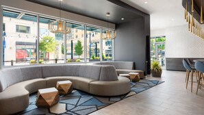 A modern lobby with a curved sofa, wooden coffee tables, and a patterned rug. Large windows offer a view of the outside. - Hyatt Place National Harbor (Oxon Hill)