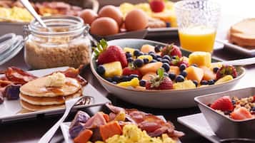 Un ricco buffet per la colazione con pancake, uova strapazzate, bacon e una varietà di frutta e verdura.