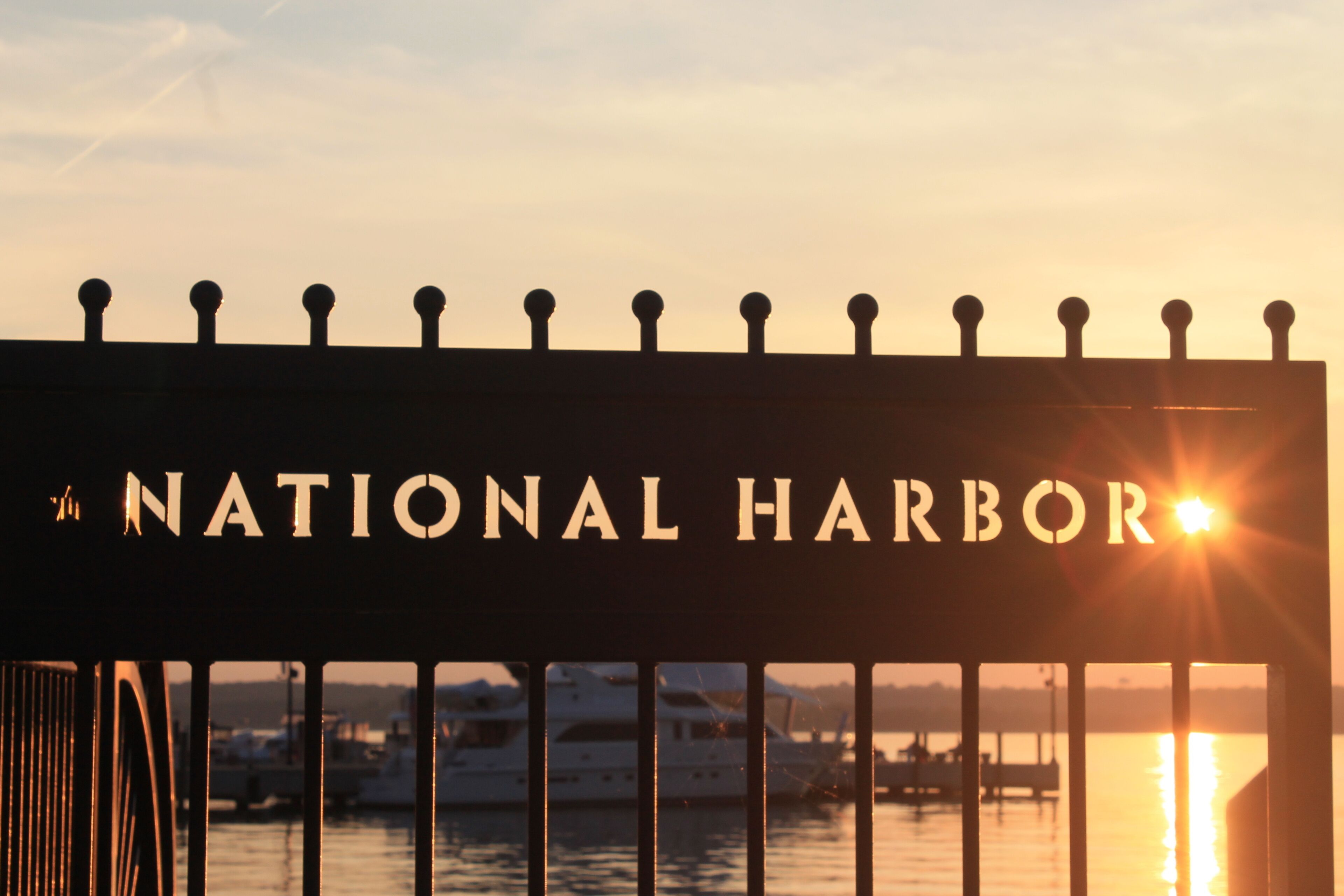 Un letrero que dice 'National Harbor' con un atardecer de fondo.