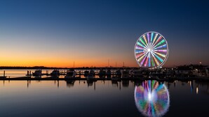 A waterfront scene with a large illuminated Ferris wheel reflecting on the water at sunset. - Hyatt Place National Harbor (Oxon Hill)
