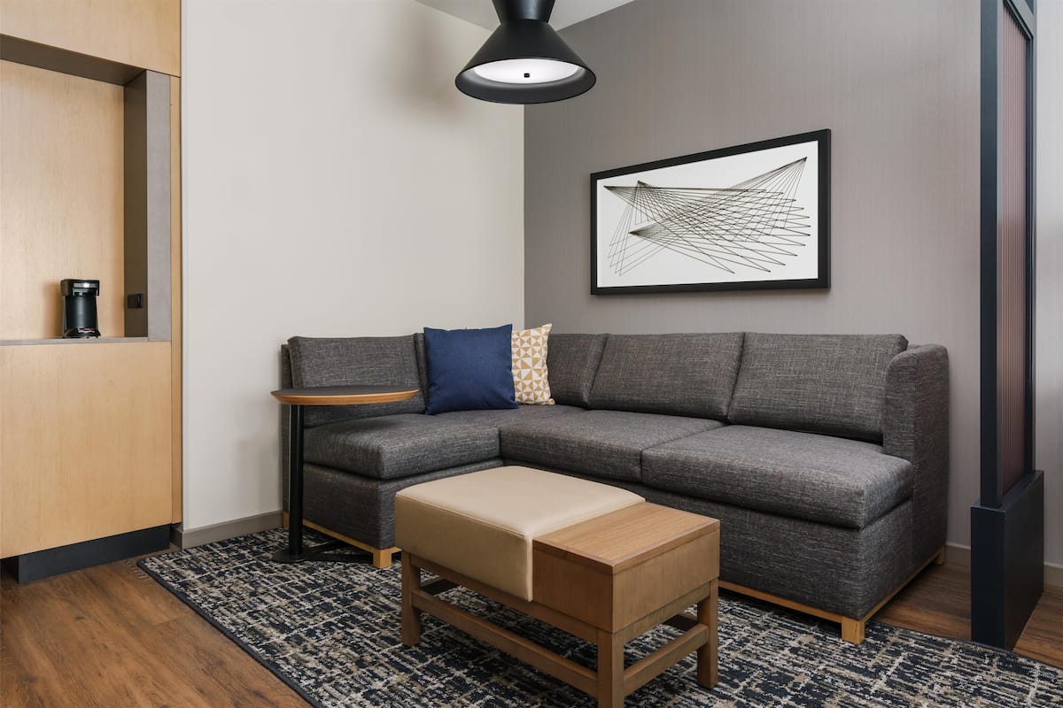 A modern living room with a gray sectional sofa, a wooden coffee table, a small side table, a black pendant light, and a framed abstract artwork on the wall.