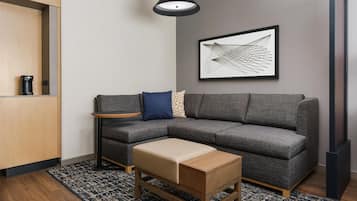 Una sala de estar moderna con un sofá seccional gris, una mesa de centro de madera, una pequeña mesita auxiliar, una lámpara colgante negra y una obra de arte abstracta enmarcada en la pared.