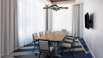 A conference room with a long table, chairs, a modern chandelier, and a flat-screen TV on the wall.
