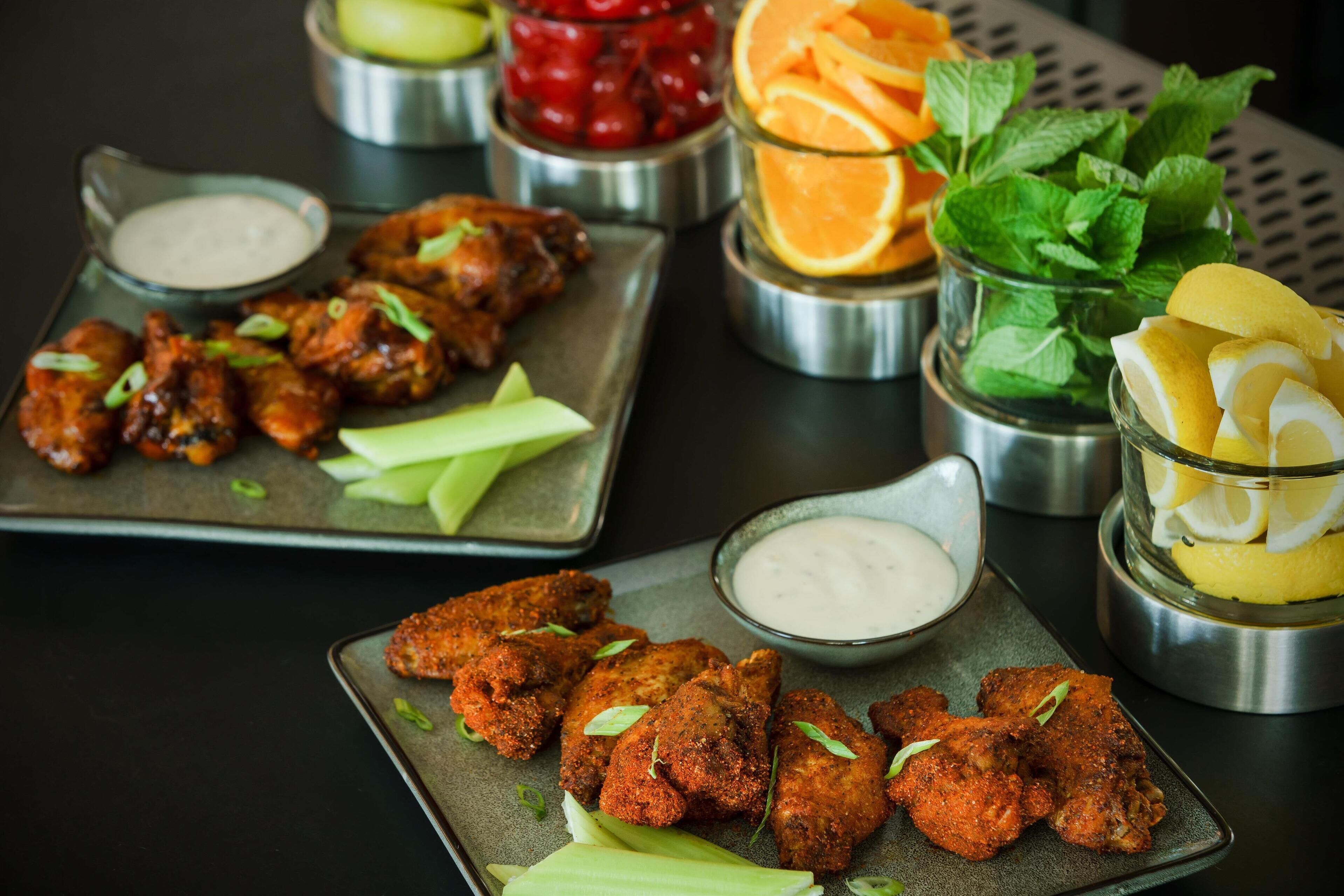 A table with food items including chicken wings, celery, and various dips.