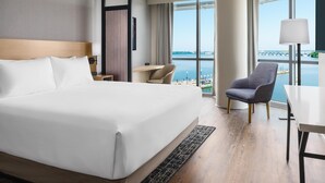 A hotel room with a large bed, a desk, a chair, and a view of a body of water with a bridge. - Hyatt Place National Harbor (Oxon Hill)