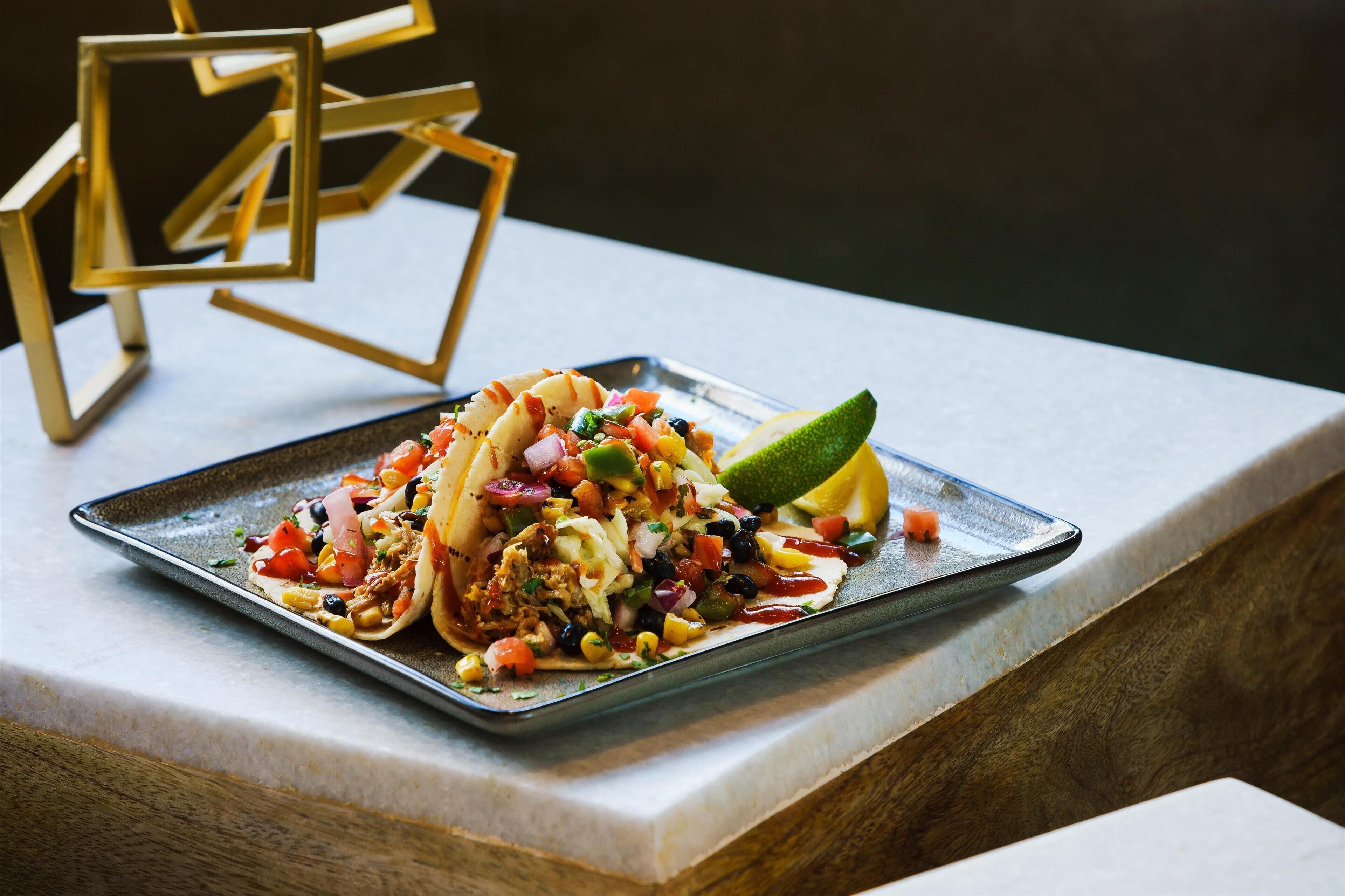 A tray of tacos with various toppings and a lime wedge on a marble surface.
