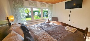 A bedroom with a bed, a TV mounted on the wall, and a window with curtains.