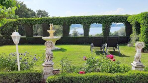 Jardí amb una font, estàtues i una vista d'un llac.