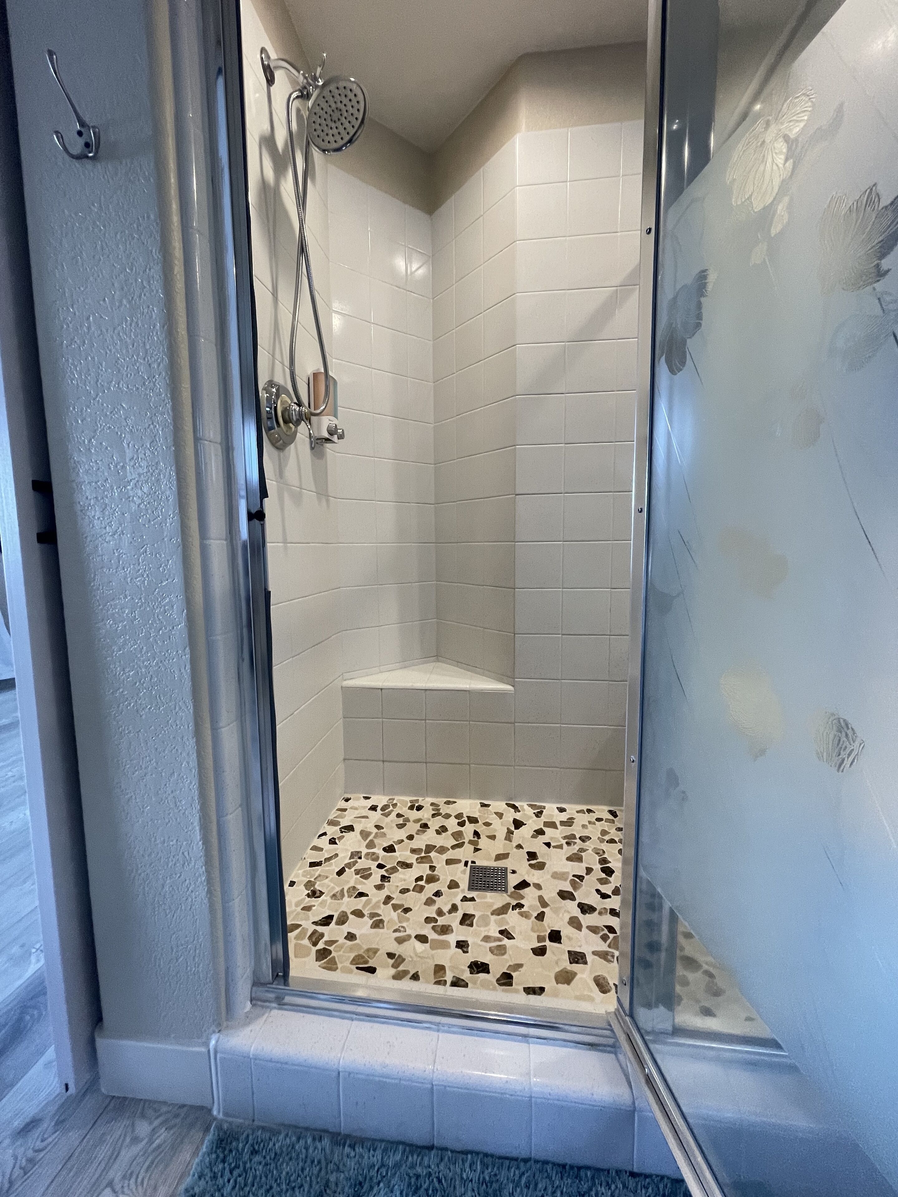 Una ducha a nivel con azulejos blancos, un cabezal de ducha y un suelo de mosaico.
