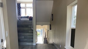 Un pasillo con piso de madera, una escalera y una puerta que da a una habitación.