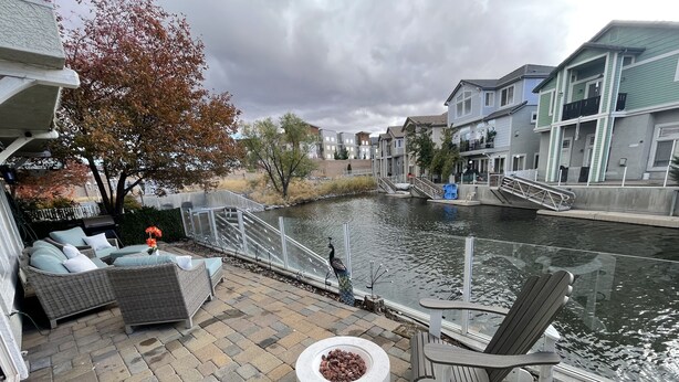 Un patio con mobiliario exterior, una fogata y vistas a un canal con edificios al fondo.