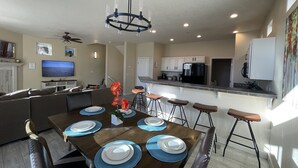 Una cocina moderna con armarios blancos, un refrigerador negro y un comedor con una mesa de madera para seis personas.