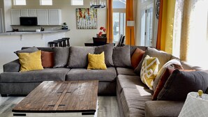 Una sala moderna con un sofá modular, una mesa de centro de madera y una cocina al fondo.
