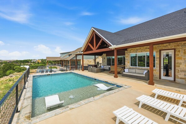 Ein Pool mit Liegestühlen, eine überdachte Terrasse und eine Fassade aus Stein.