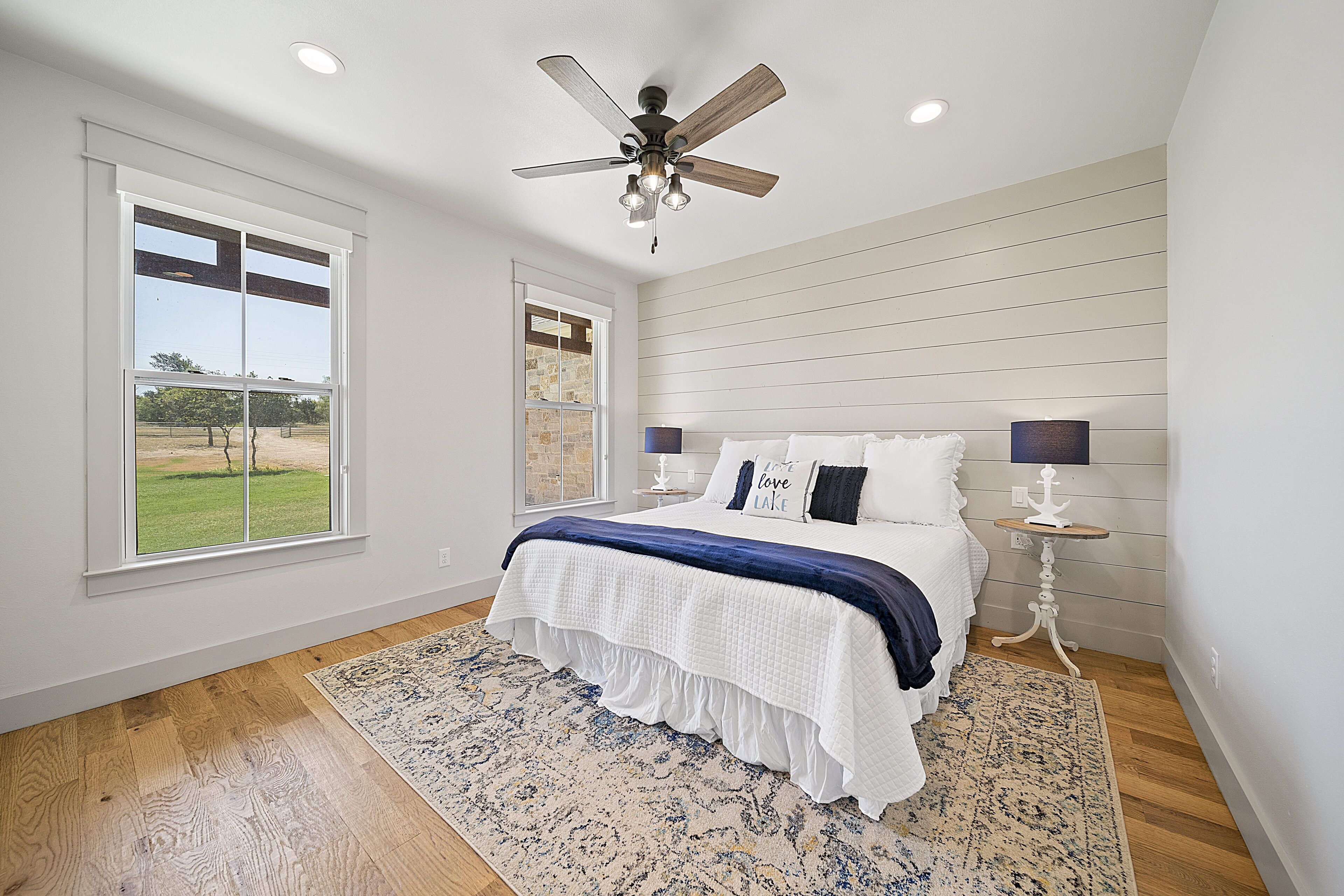 A bedroom with a large bed, a ceiling fan, and a view of a grassy area through a window.