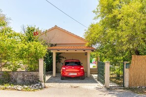 Een rode auto geparkeerd in een overdekte oprit, met een huis op de achtergrond.
