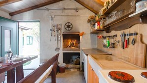 A rustic kitchen with a wood-burning stove, hanging tools, and a dining area with a bench and table. - Countryside House With Pool - Vila Šore (Dugobabe)