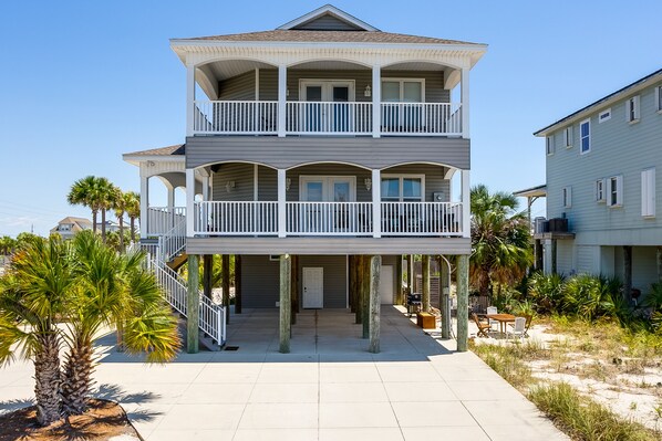 Een tweelaags strandhuis met balkon, palmbomen en een zandstrand.