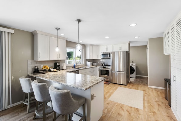 A modern kitchen with a central island, bar stools, stainless steel appliances, and a view to the outdoors.
