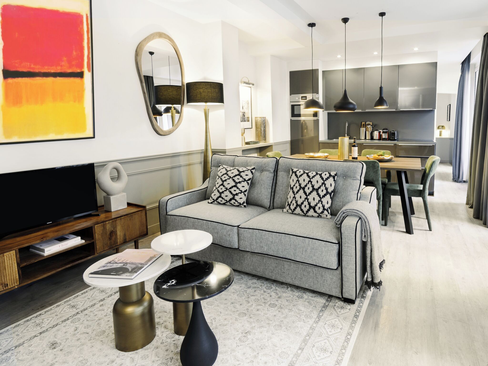 Una sala de estar moderna con un sofá gris, un televisor de pantalla plana y un comedor con mesa y sillas.