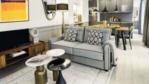 Een moderne woonkamer met een grijze bank, een flatscreen televisie en een eethoek met een tafel en stoelen.