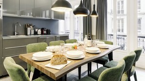 Een moderne keuken met een eetgedeelte, met een houten tafel voor zes personen, groene bekleden stoelen en hanglampen.