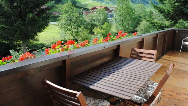 A wooden deck with a table and chairs, surrounded by a flower bed with red flowers. - Naturhaus Andrea Rose with special hiking experiences Holiday apartments (Grossarl)