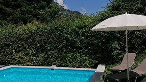 A swimming pool with clear blue water, surrounded by lush greenery and a view of a mountain. - Naturhaus Andrea Rose with special hiking experiences Holiday apartments (Grossarl)