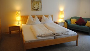 A neatly made bed with white linens, two bedside tables with lamps, a green sofa with cushions, and a painting of a rose on the wall. - Naturhaus Andrea Rose with special hiking experiences Holiday apartments (Grossarl)