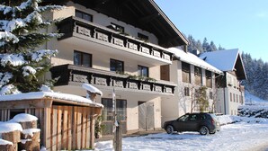 A multi-story building with balconies, a car parked in front, and snow on the ground. - Naturhaus Andrea Rose with special hiking experiences Holiday apartments (Grossarl)
