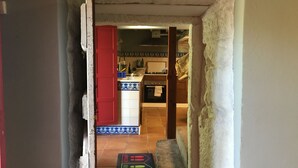 A narrow hallway leading to a kitchen with a red door, a tiled backsplash, and a visible stove. - Beautiful stone house in tranquil, rural setting (Pontevedra)