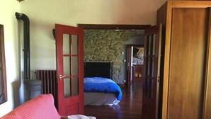 A room with a red door, a bed with a blue bedspread, a wooden floor, and a stone wall. - Beautiful stone house in tranquil, rural setting (Pontevedra)