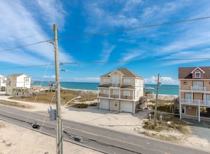 Ein Küstengebiet mit einem zweistöckigen Haus, Blick auf den Strand und einer Straße im Vordergrund.